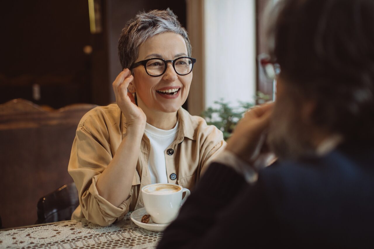 A smiling woman chatting over coffee with a friend, comfortable and free of jaw pain