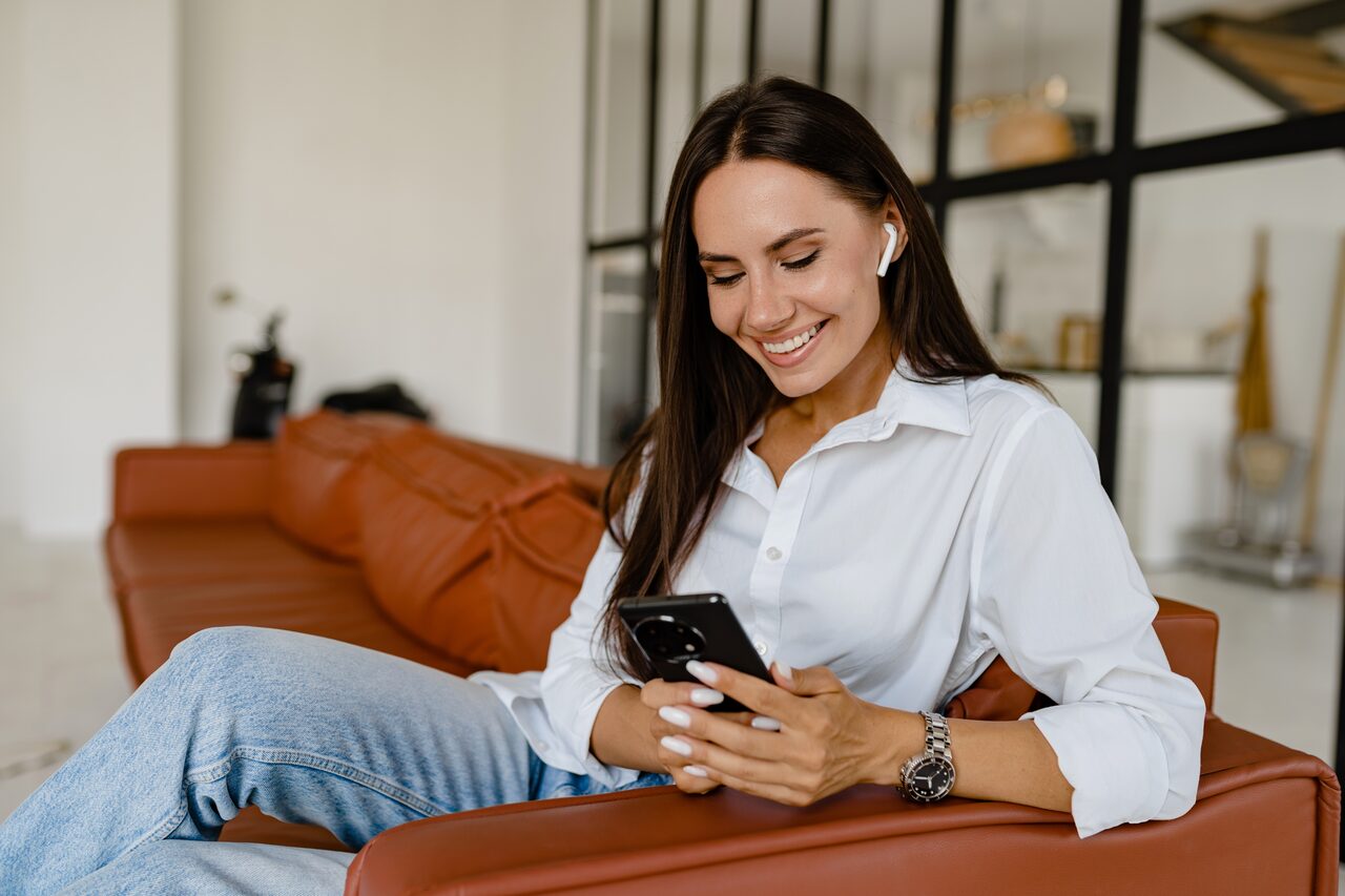 A smiling woman relaxing on her couch while using her phone