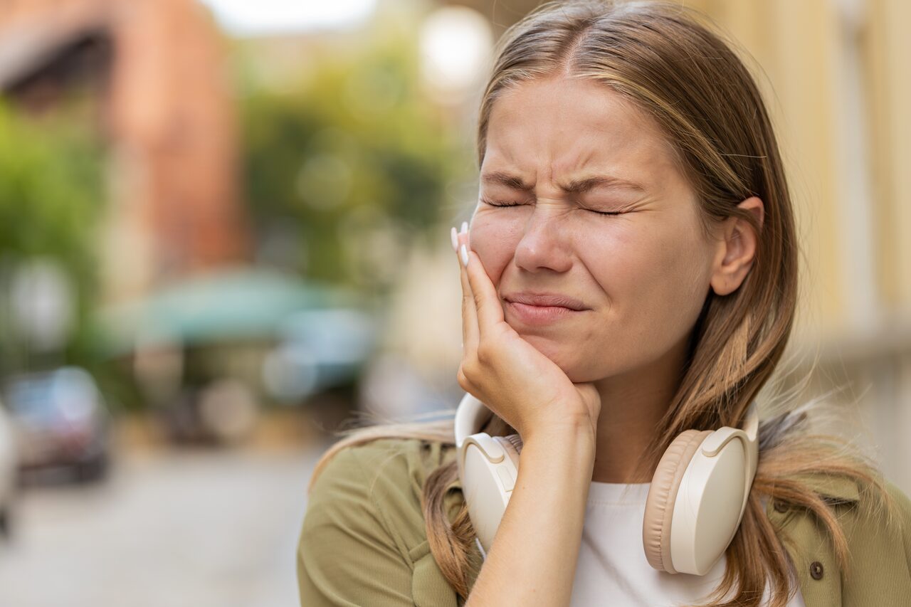 A woman holding the side of her jaw in pain, over the masseter muscle